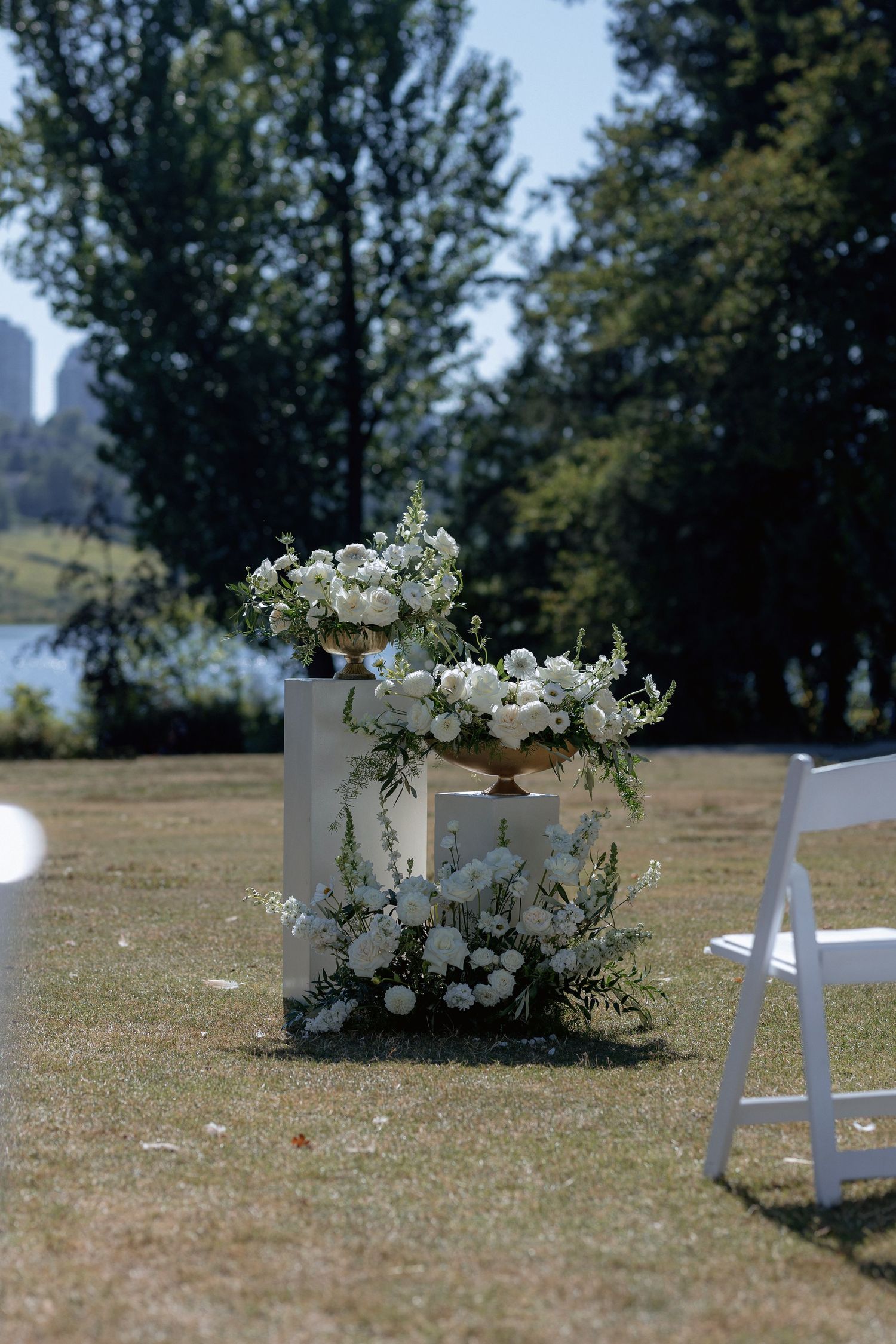 White garden chairs and floral decorations set up on grass for an outdoor ceremony.