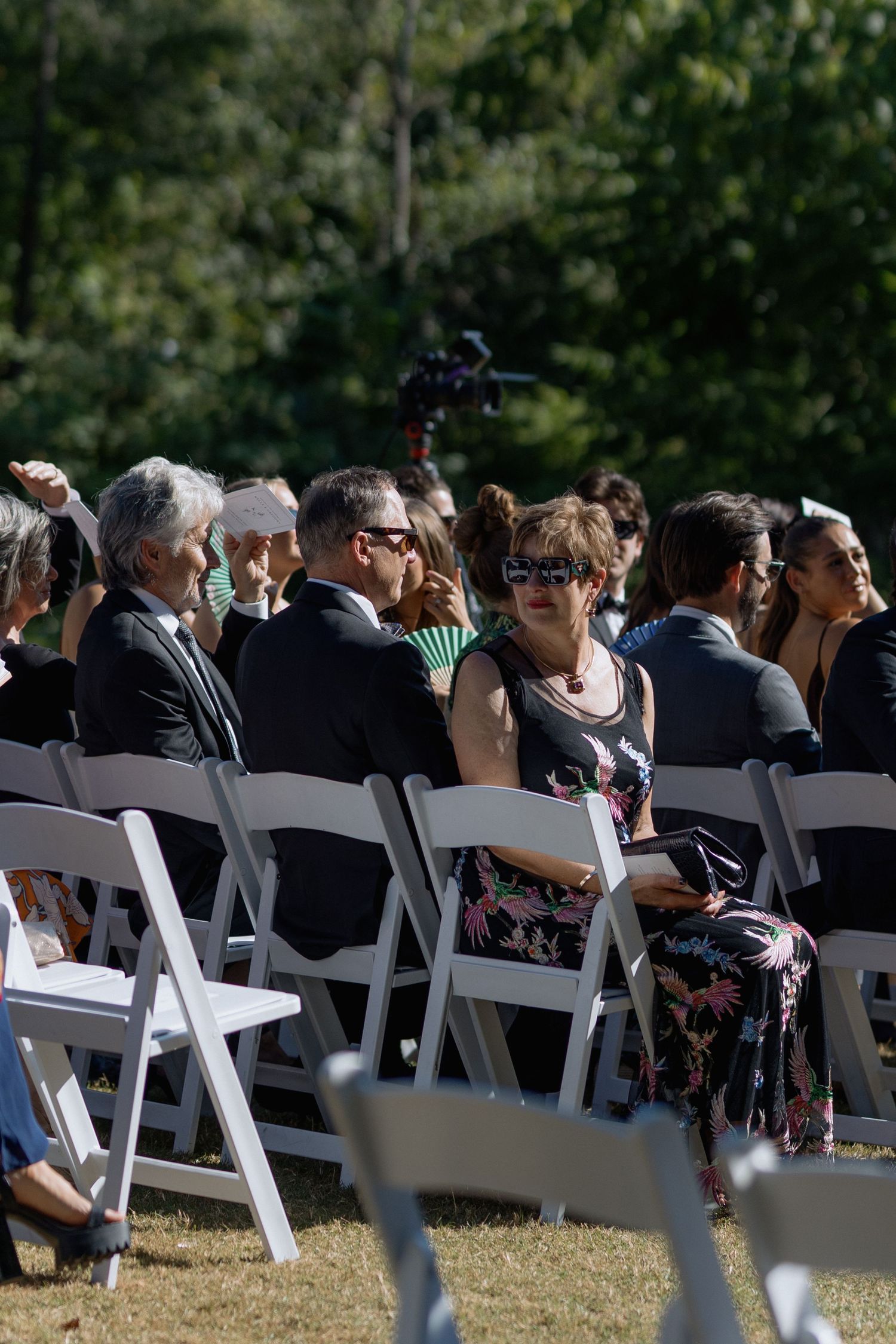 Wedding guests seated in rows of white folding chairs at outdoor ceremony.
