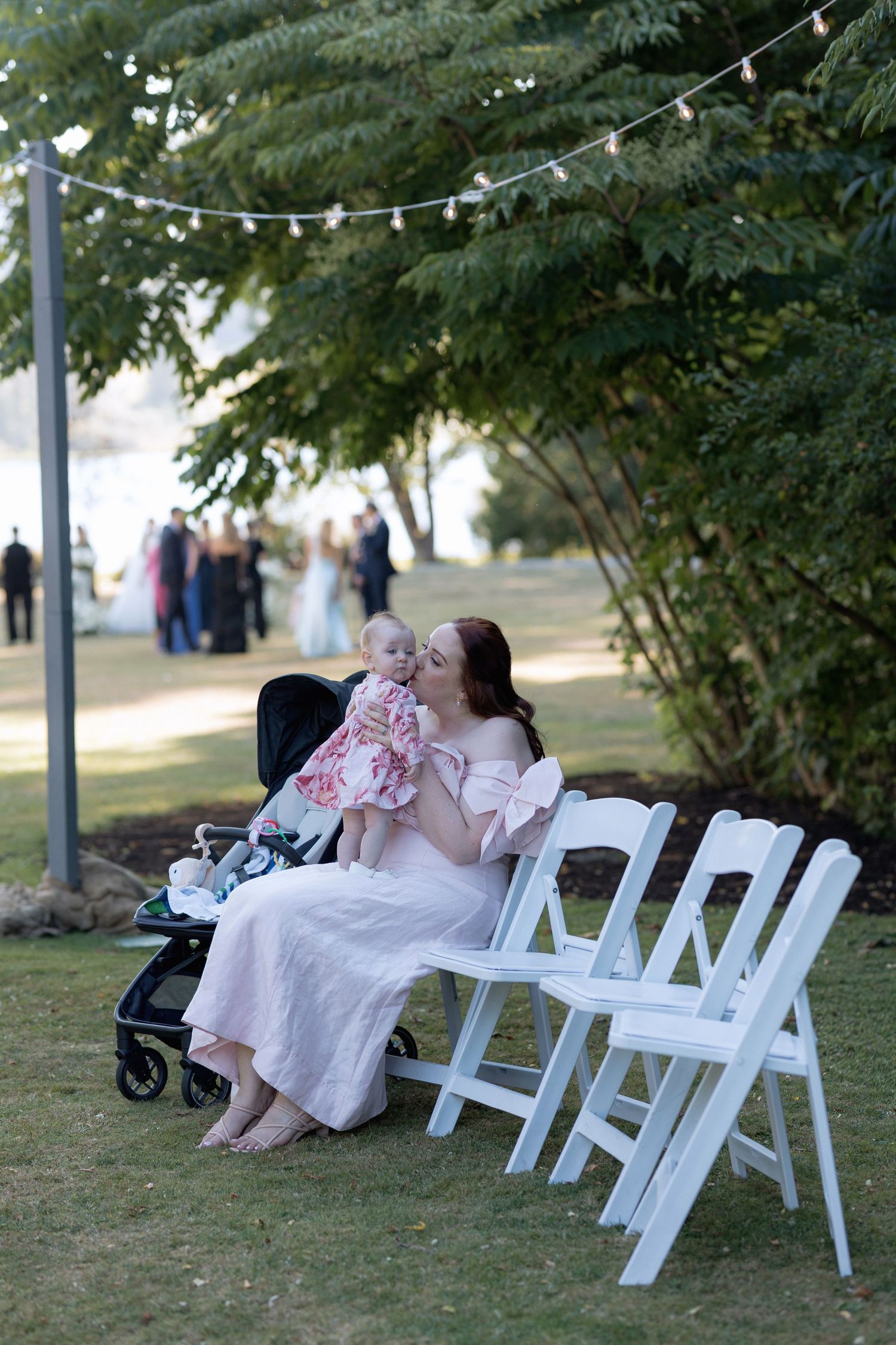 White folding chairs line a garden path under string lights at an outdoor wedding venue.