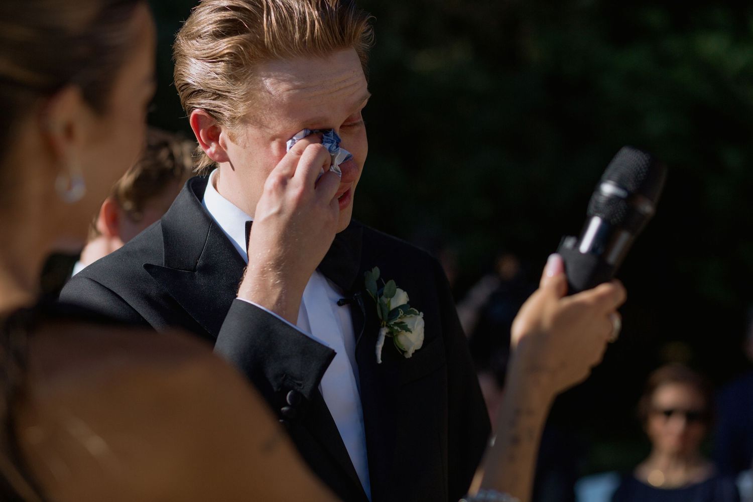 Attendees at a formal outdoor event react emotionally while reading from papers.