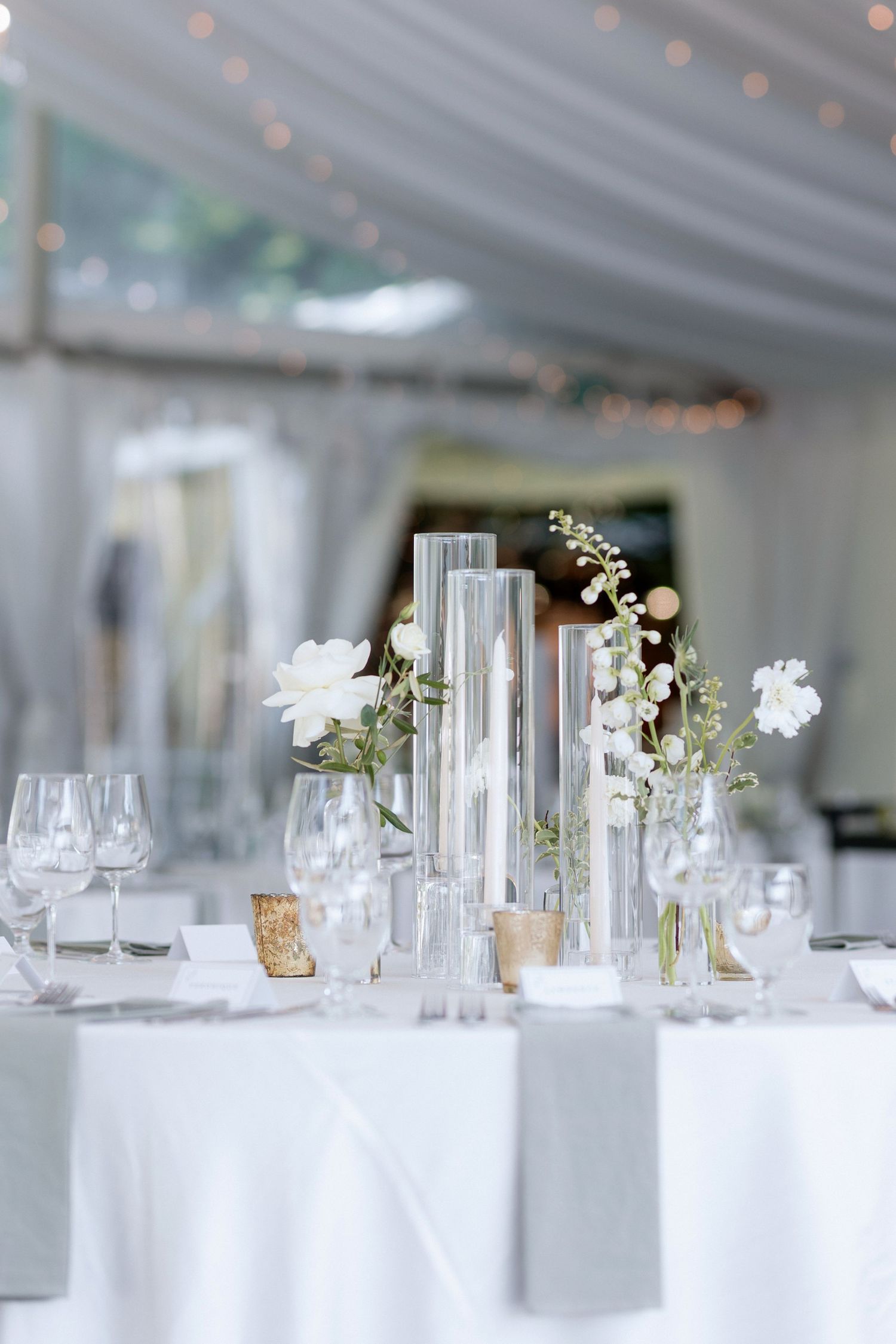 White reception tables with tall glass vases and delicate floral centerpieces.