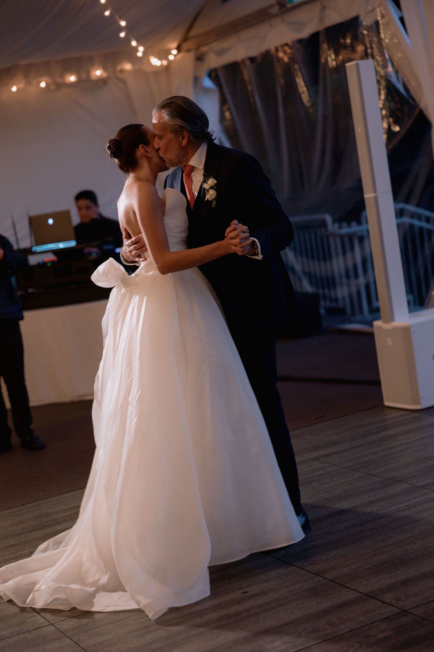 Romantic dance moment in a white wedding gown and formal suit under twinkling lights.