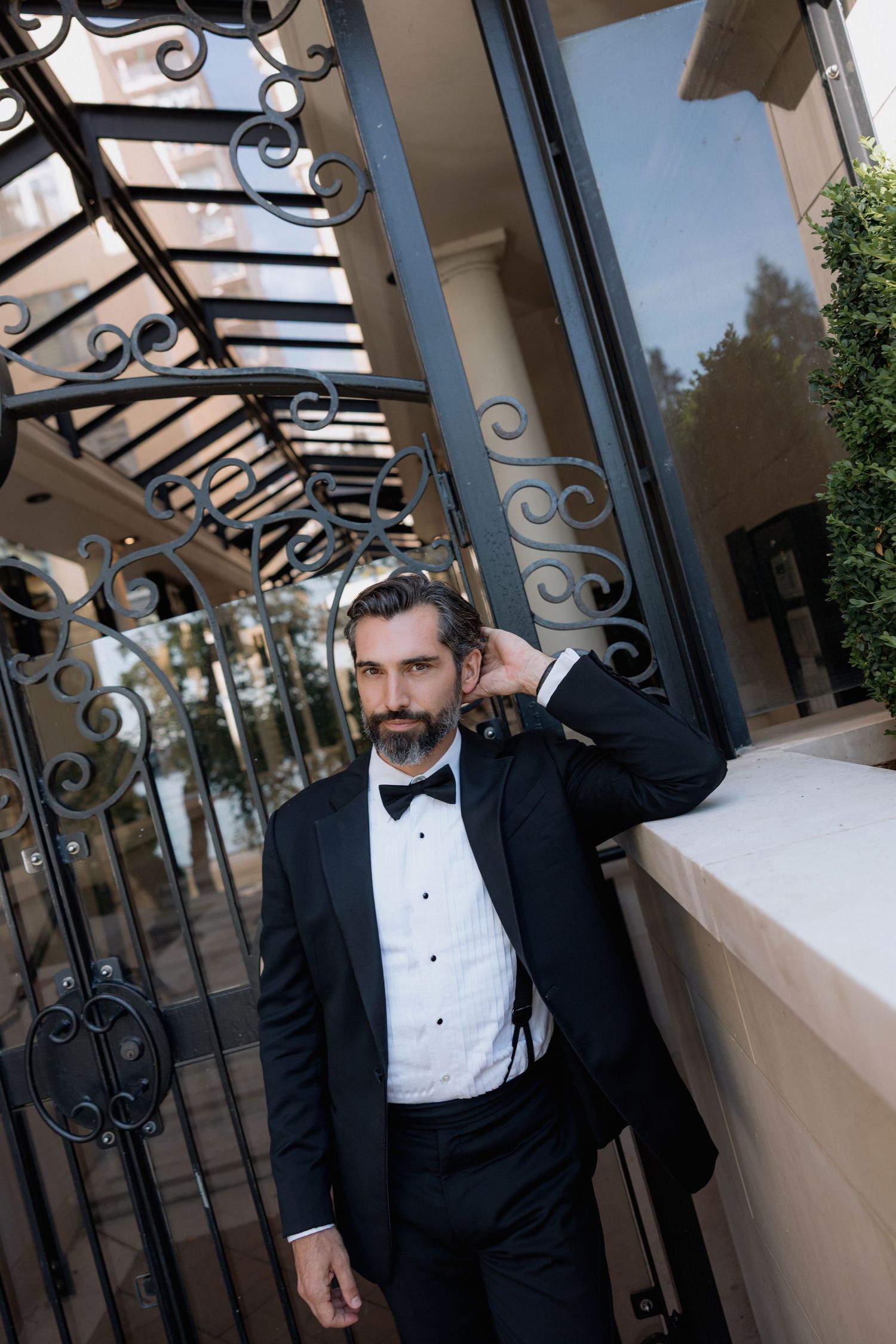 A groom in classic black tuxedo poses against ornate iron railings.