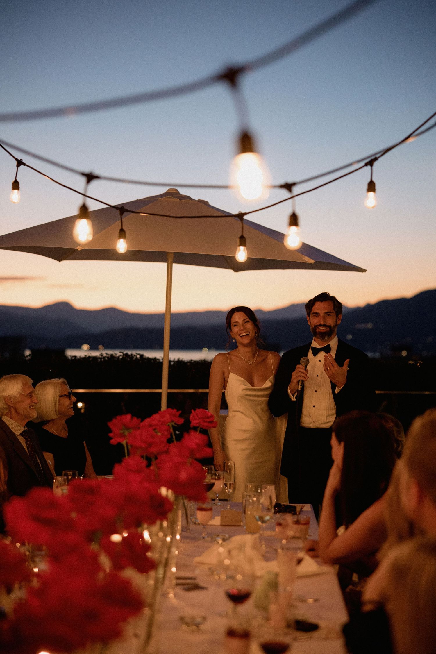 Outdoor evening reception with string lights and mountain views at sunset.