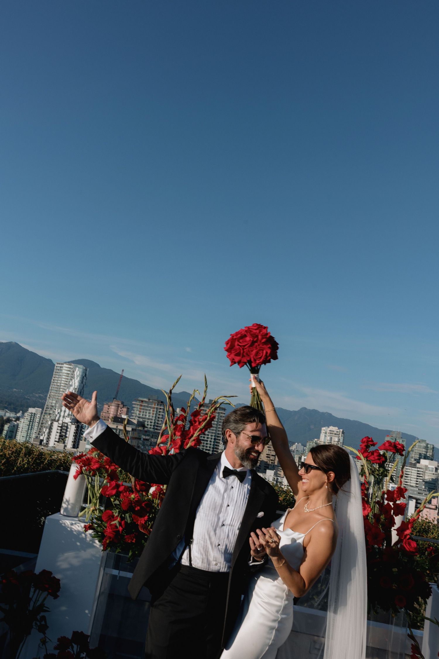Celebratory moment at rooftop wedding with city skyline and mountains in background.
