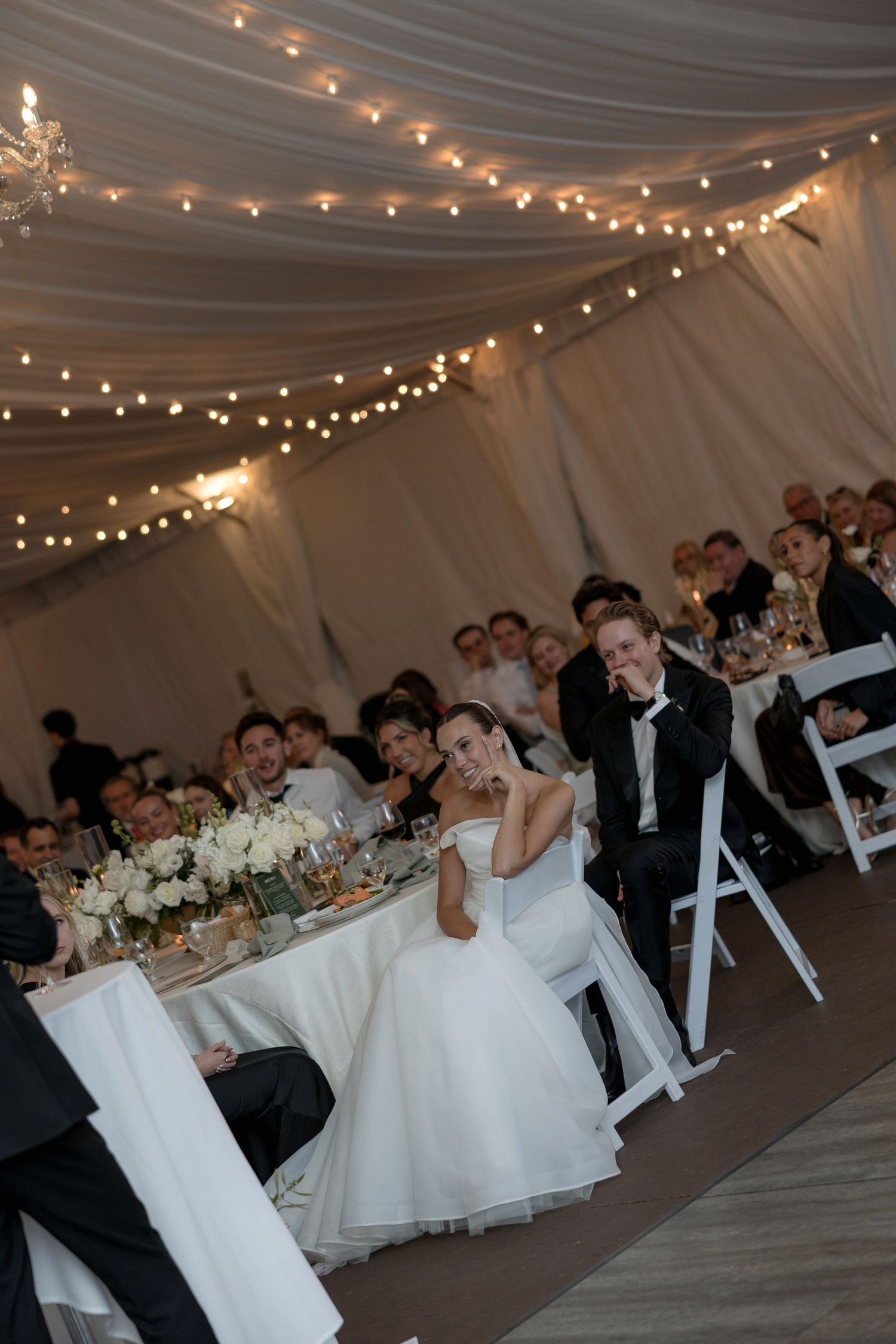 Wedding reception under draped ceiling with string lights and elegant table settings.