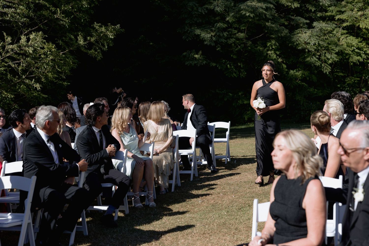 Outdoor wedding venue with white chairs and guests in formal attire gathering before ceremony.