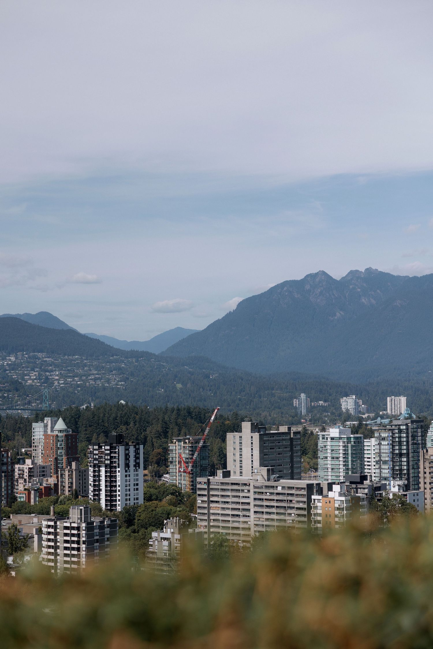 Panoramic cityscape of Vancouver with high-rise buildings against a backdrop of mountains and cloudy skies.