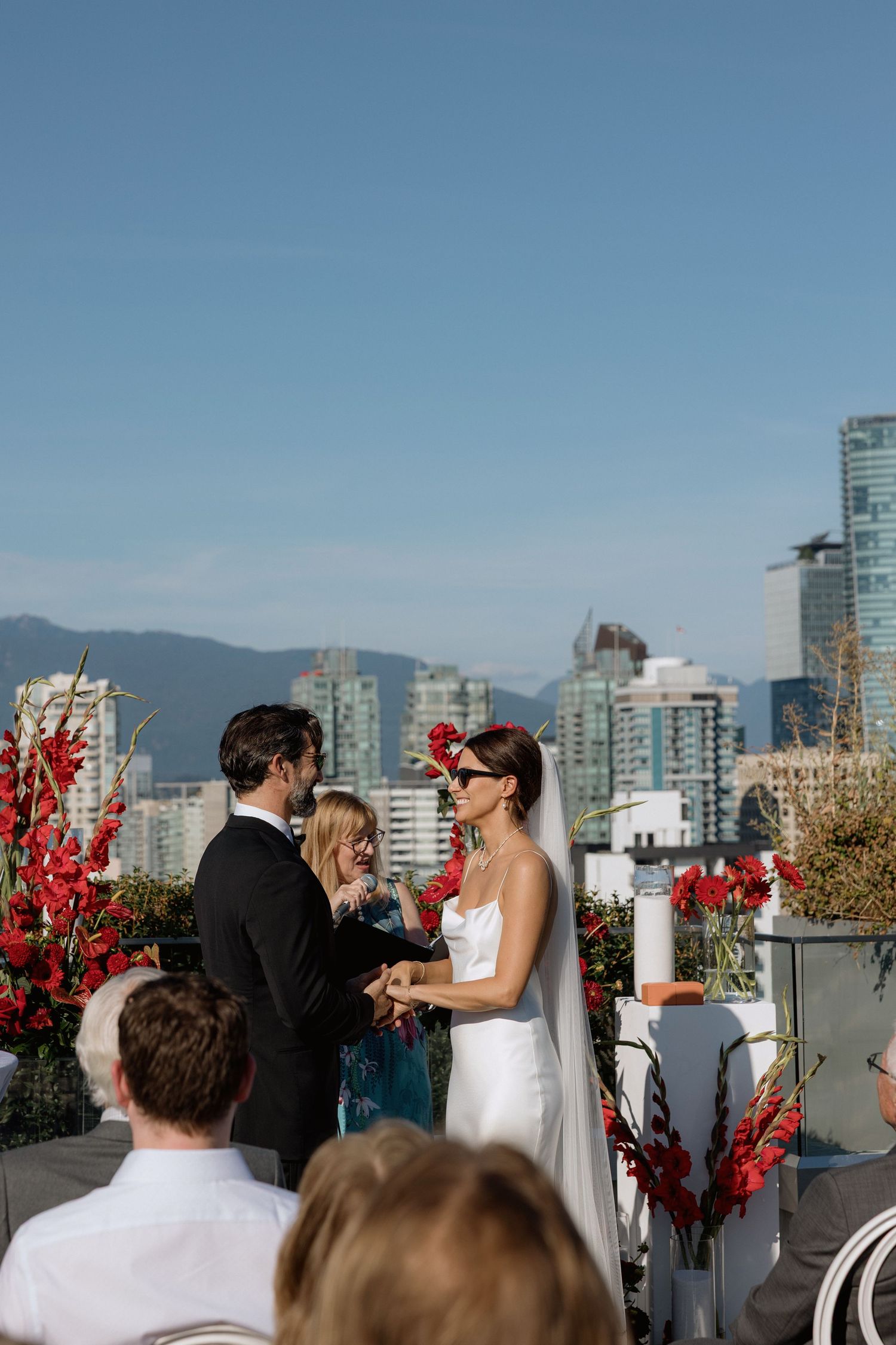 Rooftop wedding ceremony with red floral decorations and city skyline views.