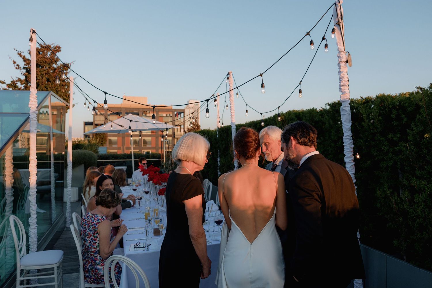 Evening rooftop reception with string lights and urban backdrop.