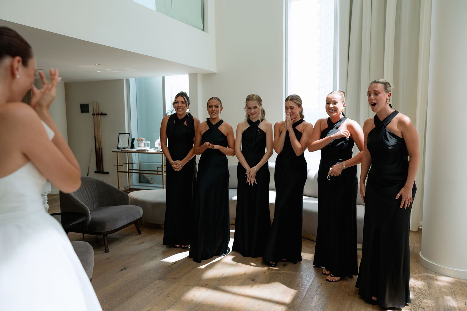 A row of people in matching black attire gather in a sunlit room with hardwood floors.