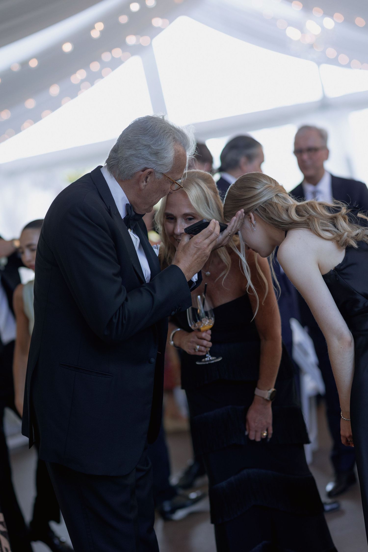 Wedding guests socializing and sharing intimate conversations under a white tent with string lights.