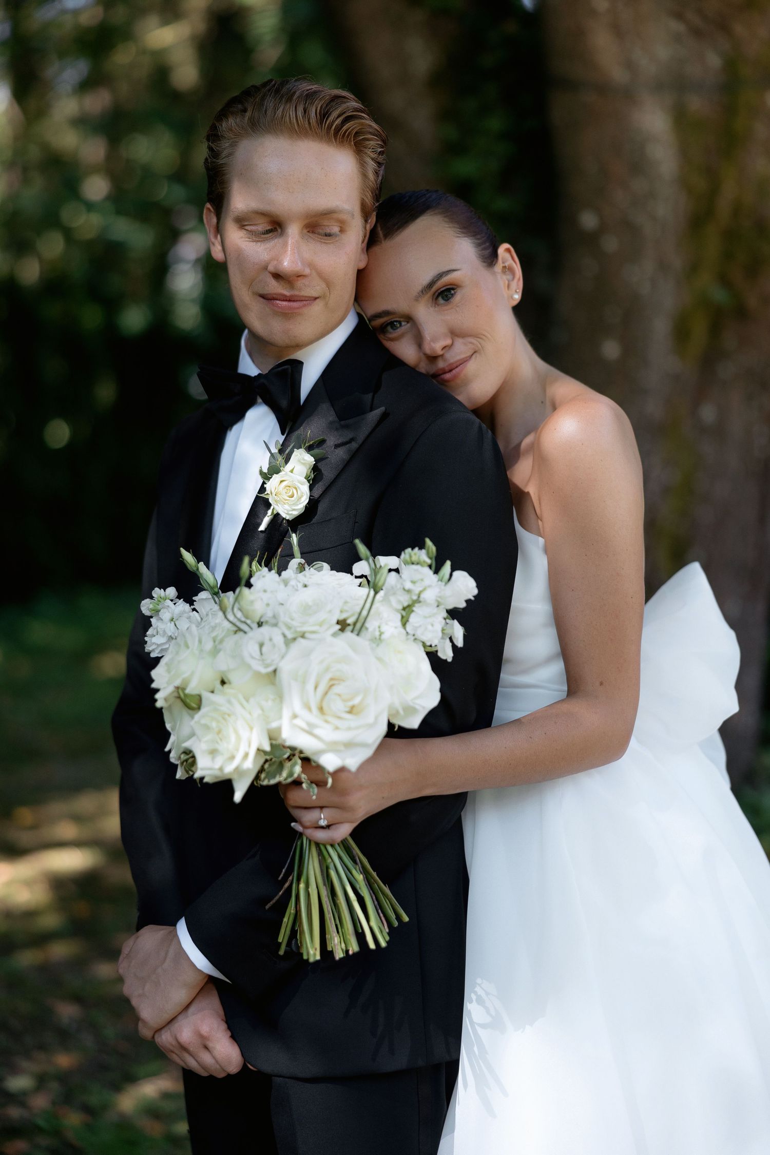 Romantic wedding portrait of couple with white bouquet in outdoor garden setting.