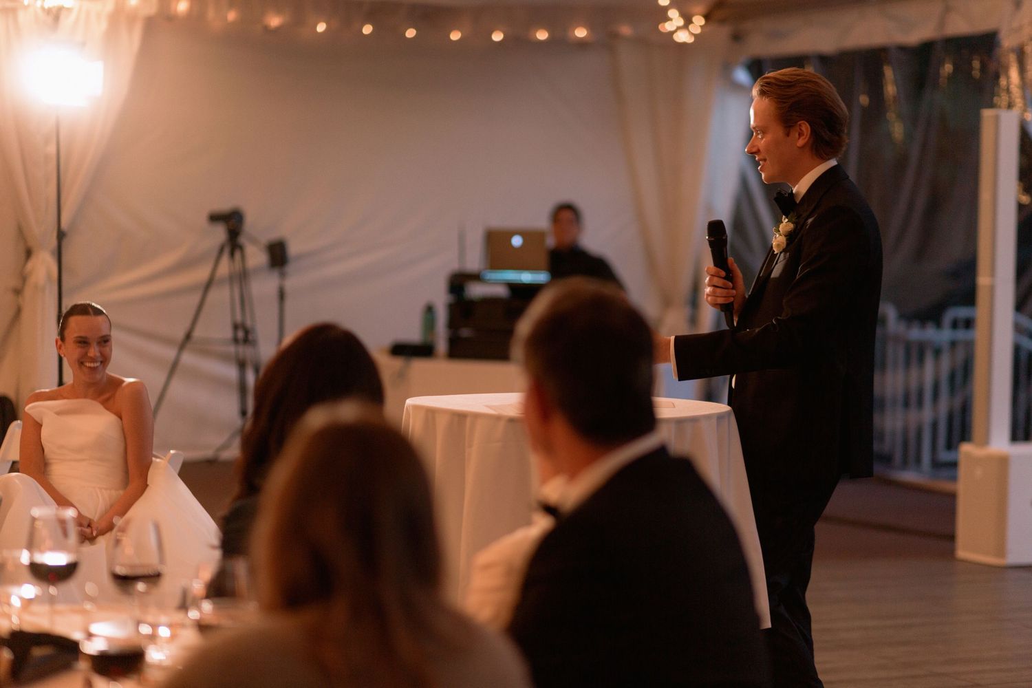 Wedding reception under a white tent with string lights and chandeliers.