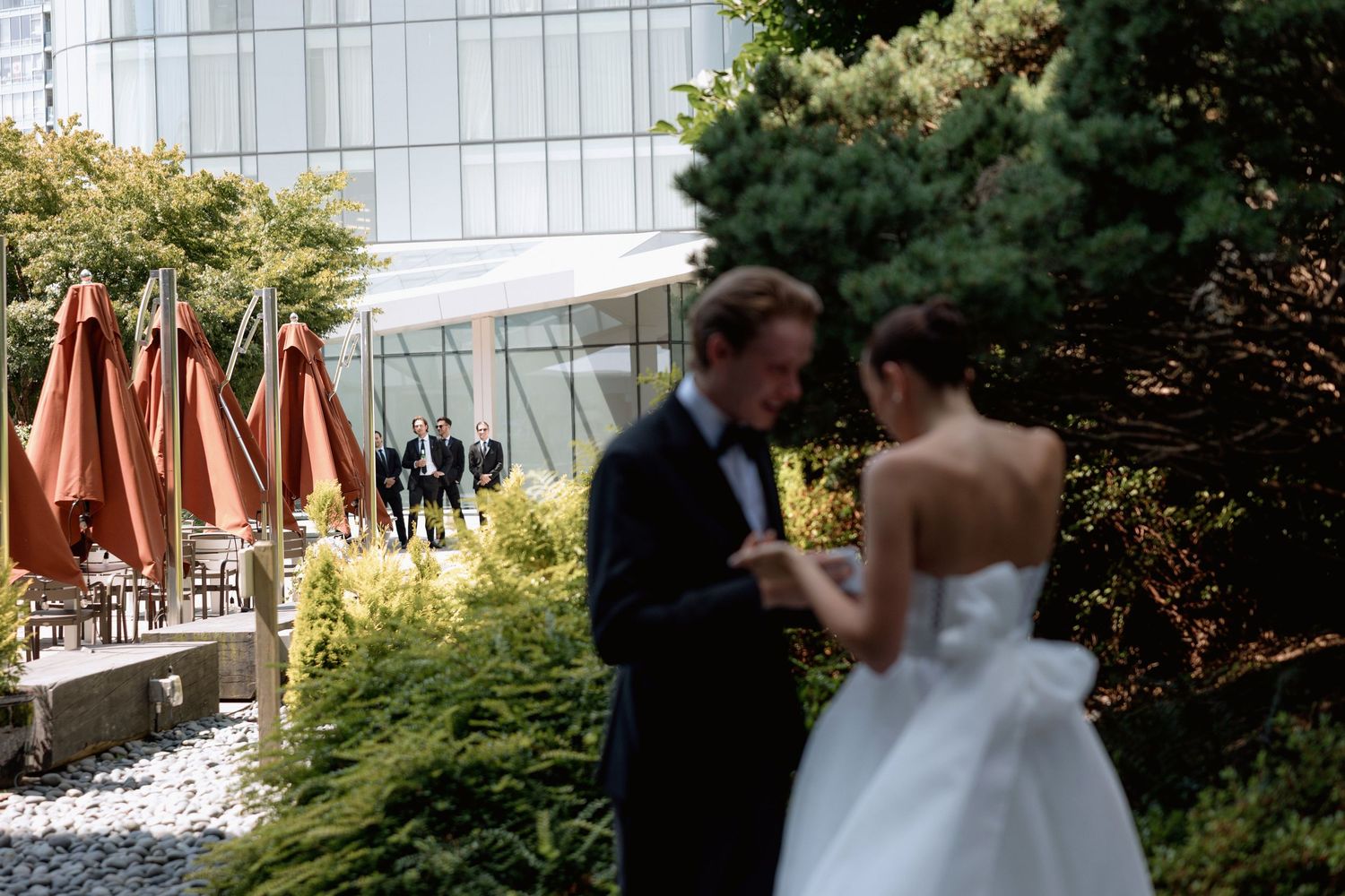 A wedding couple shares an intimate moment with orange umbrellas visible in the background.