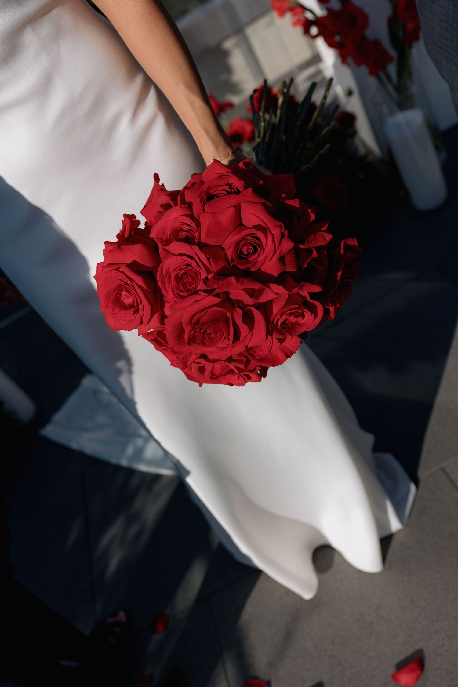 Close-up of a stunning red rose bouquet against a white wedding dress.
