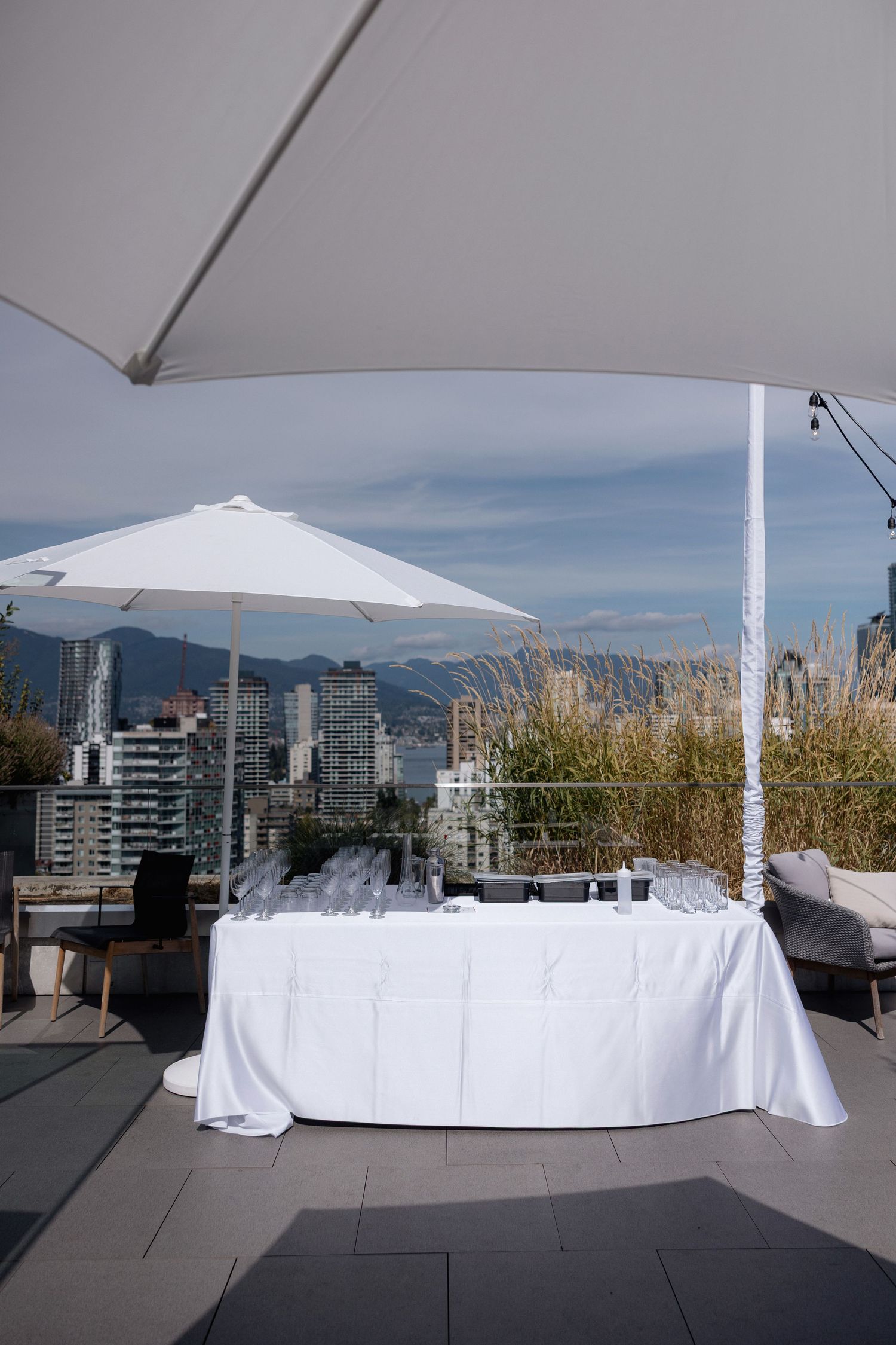 White event setup with umbrellas on a rooftop patio overlooking Vancouver's skyline and mountains.
