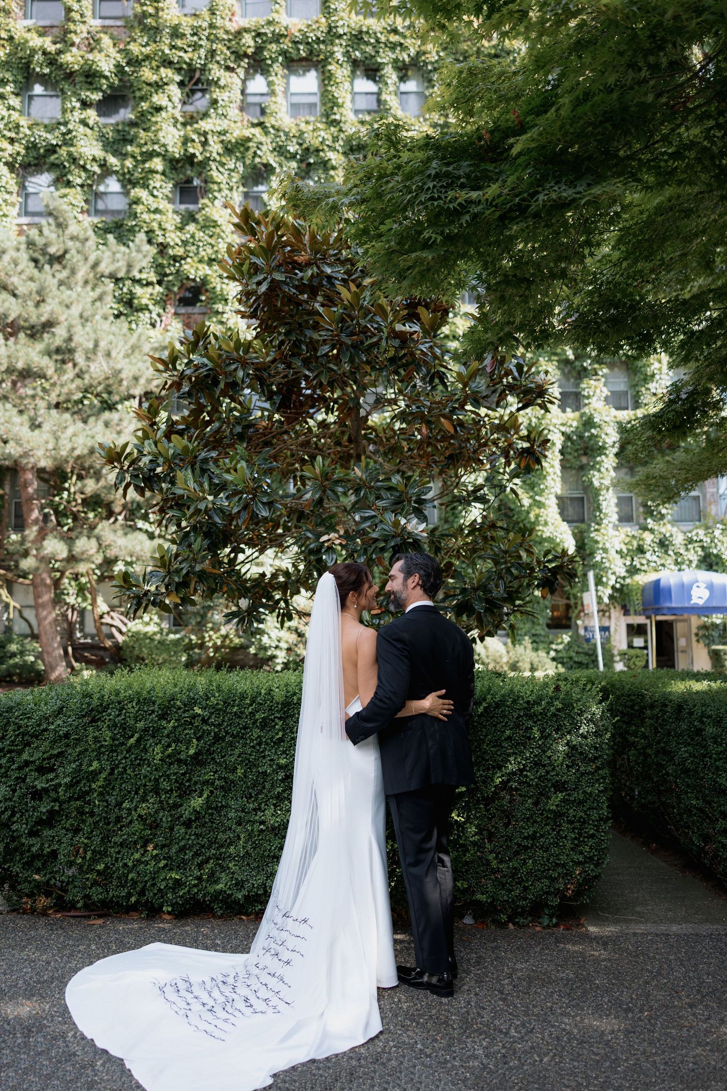 Newlyweds sharing an intimate moment in a garden setting with lush greenery in front of the Sylvia Hotel in Vancouver