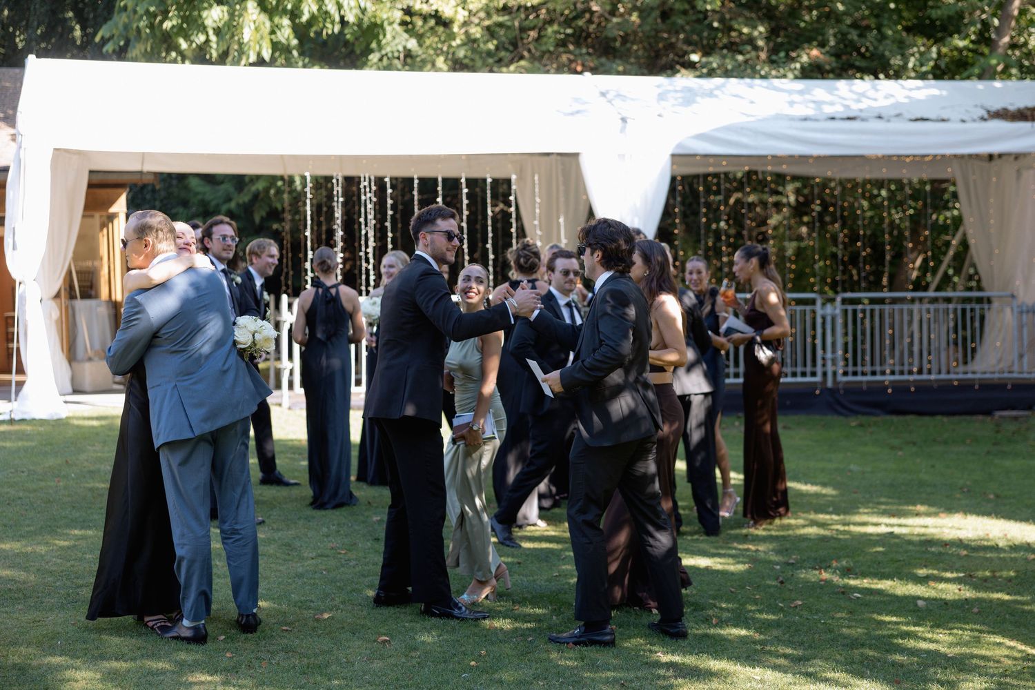 Wedding guests mingling and dancing at an outdoor tented reception.