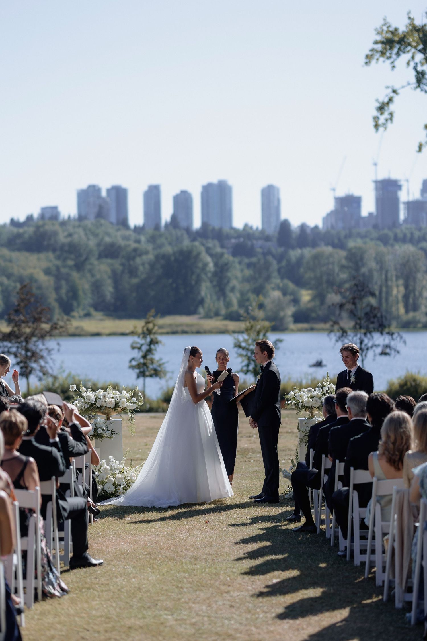 Wedding ceremony setup with white chairs and floral arrangements against a backdrop of city buildings and water.