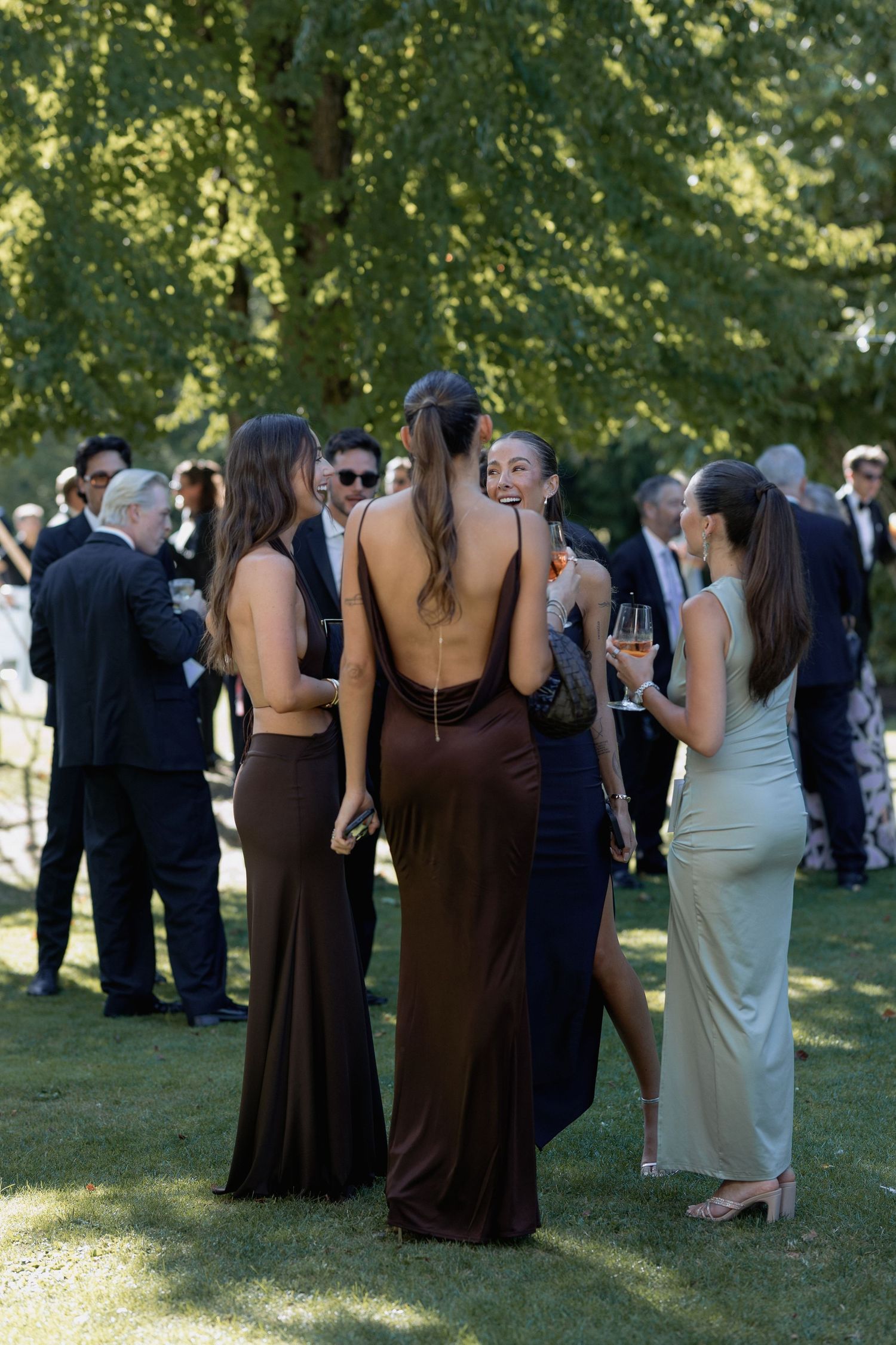 Elegantly dressed guests mingling at an outdoor wedding reception on a sunny day.