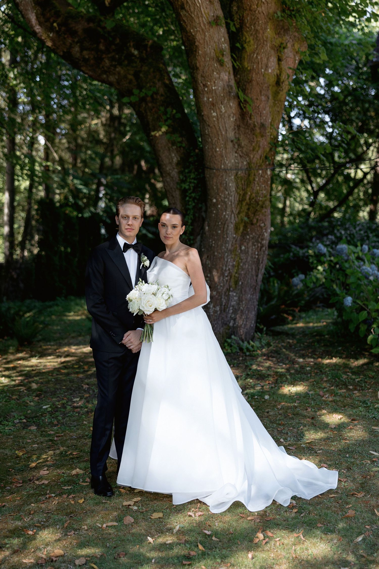 Wedding couple poses for romantic portraits in a wooded setting with dappled sunlight.