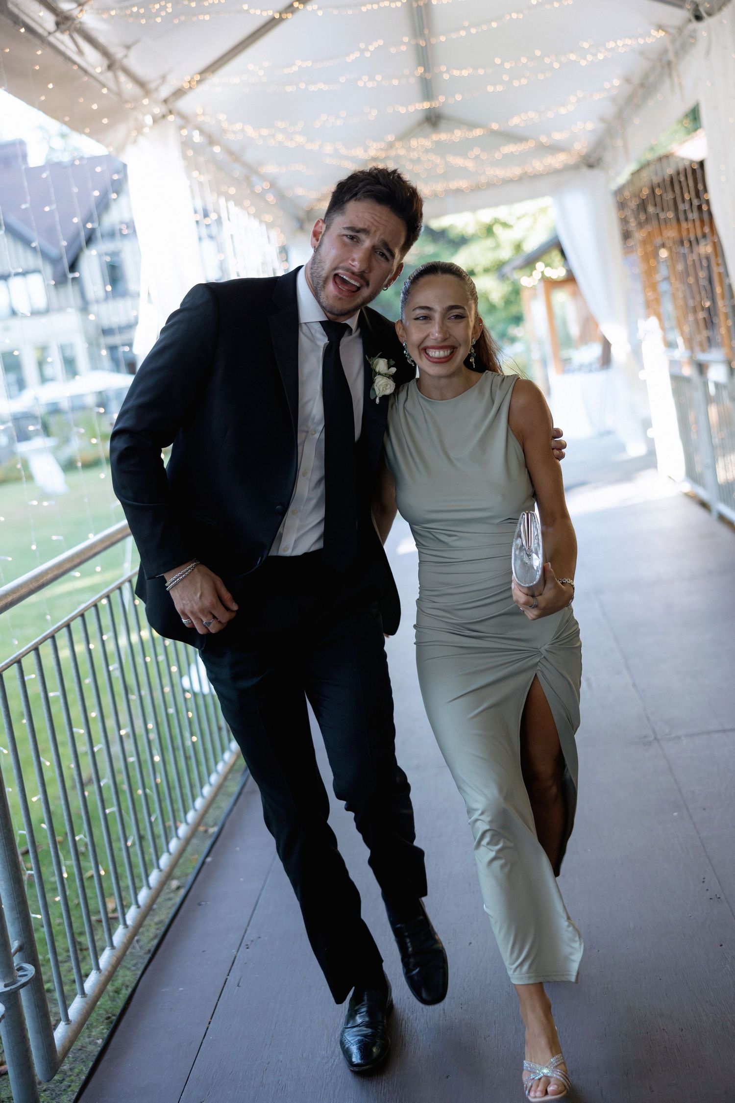 Couple in formal attire running playfully through a covered walkway during a wedding photoshoot.