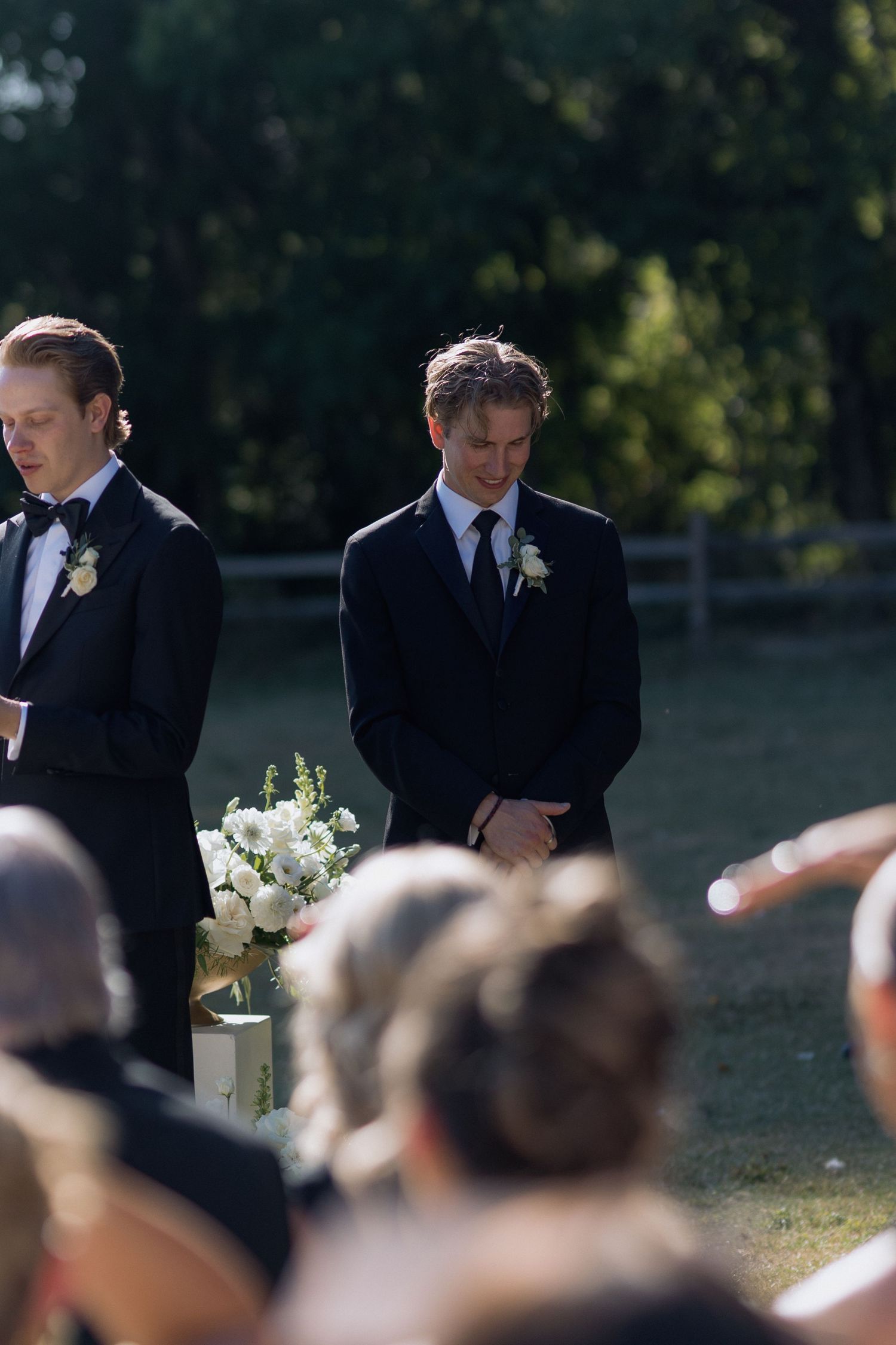 Groomsmen in black suits standing in formation during an outdoor wedding ceremony.