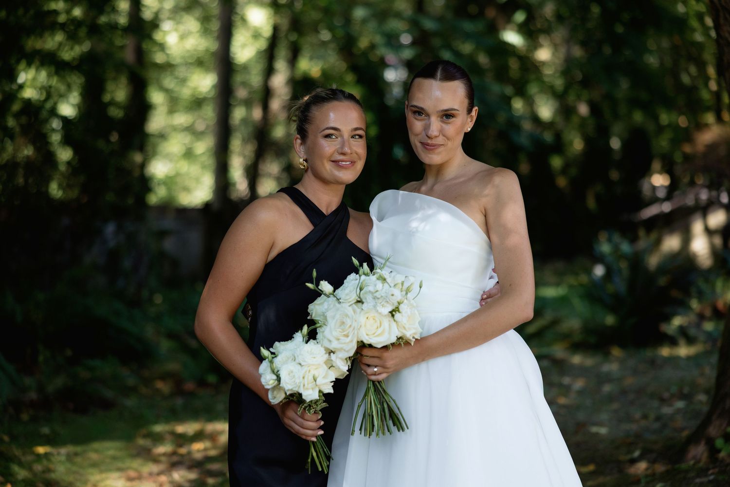 Intimate wedding photo with two people embracing while holding white bouquets in a wooded setting.