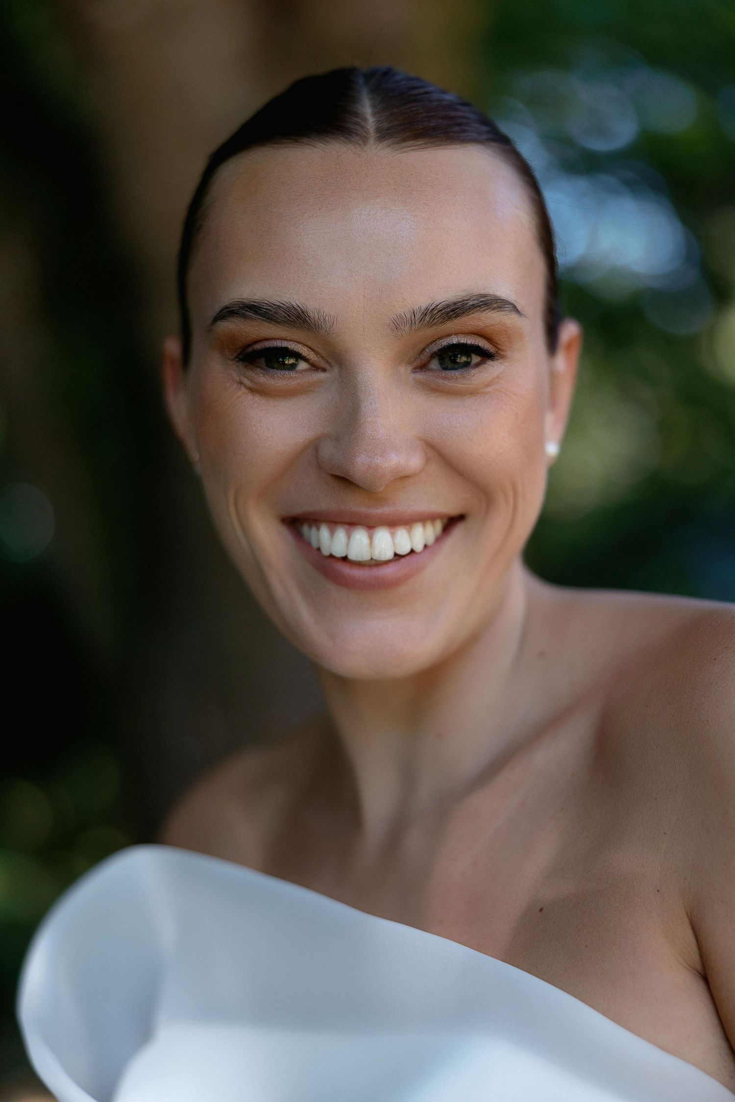 Close up portrait of person in white wedding dress smiling brightly.