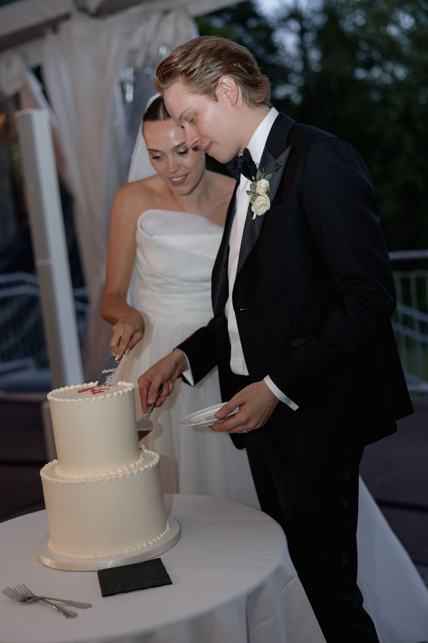 A couple sharing a playful moment while cutting their wedding cake outdoors.