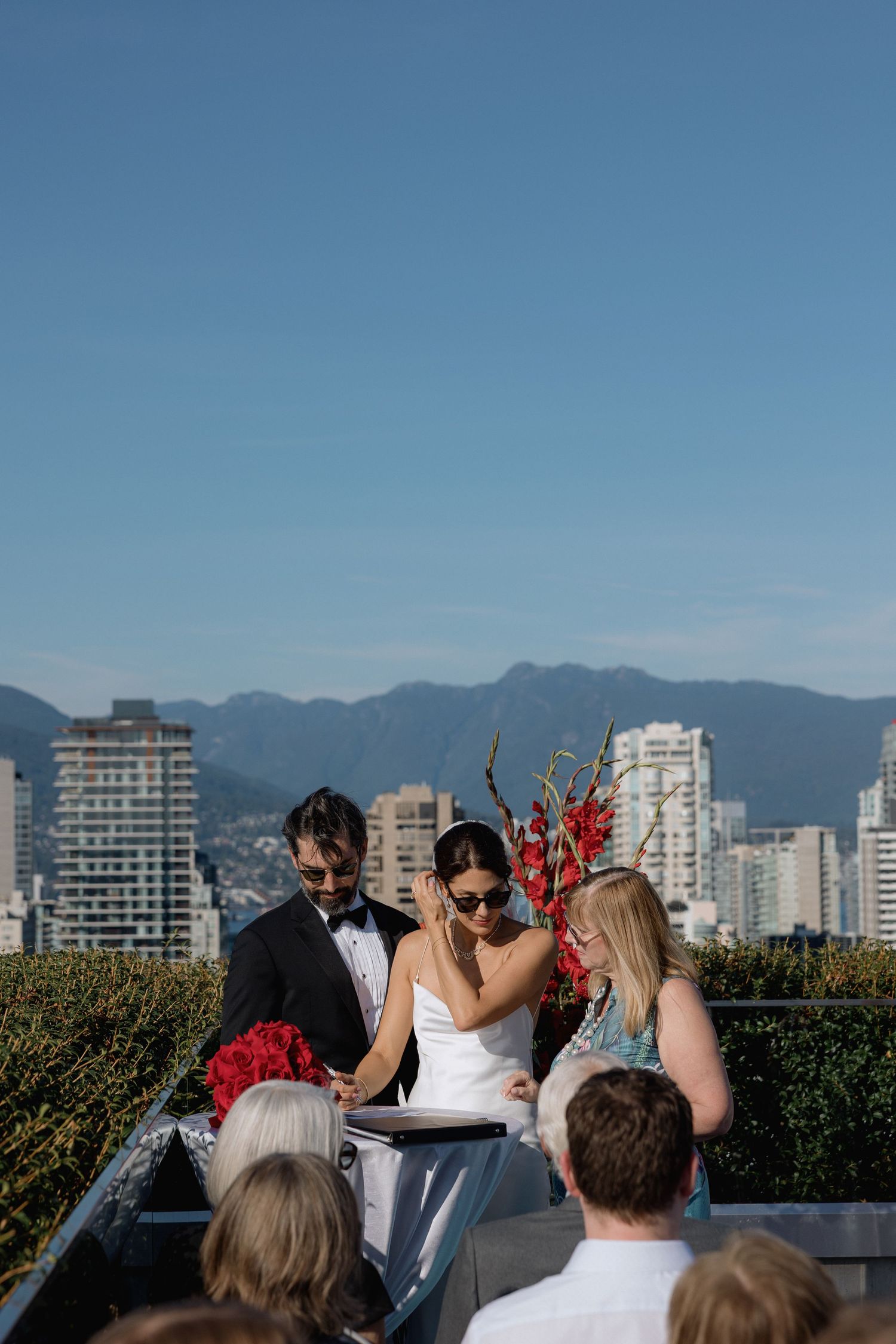Outdoor rooftop wedding ceremony with Vancouver city skyline and mountains in the background.