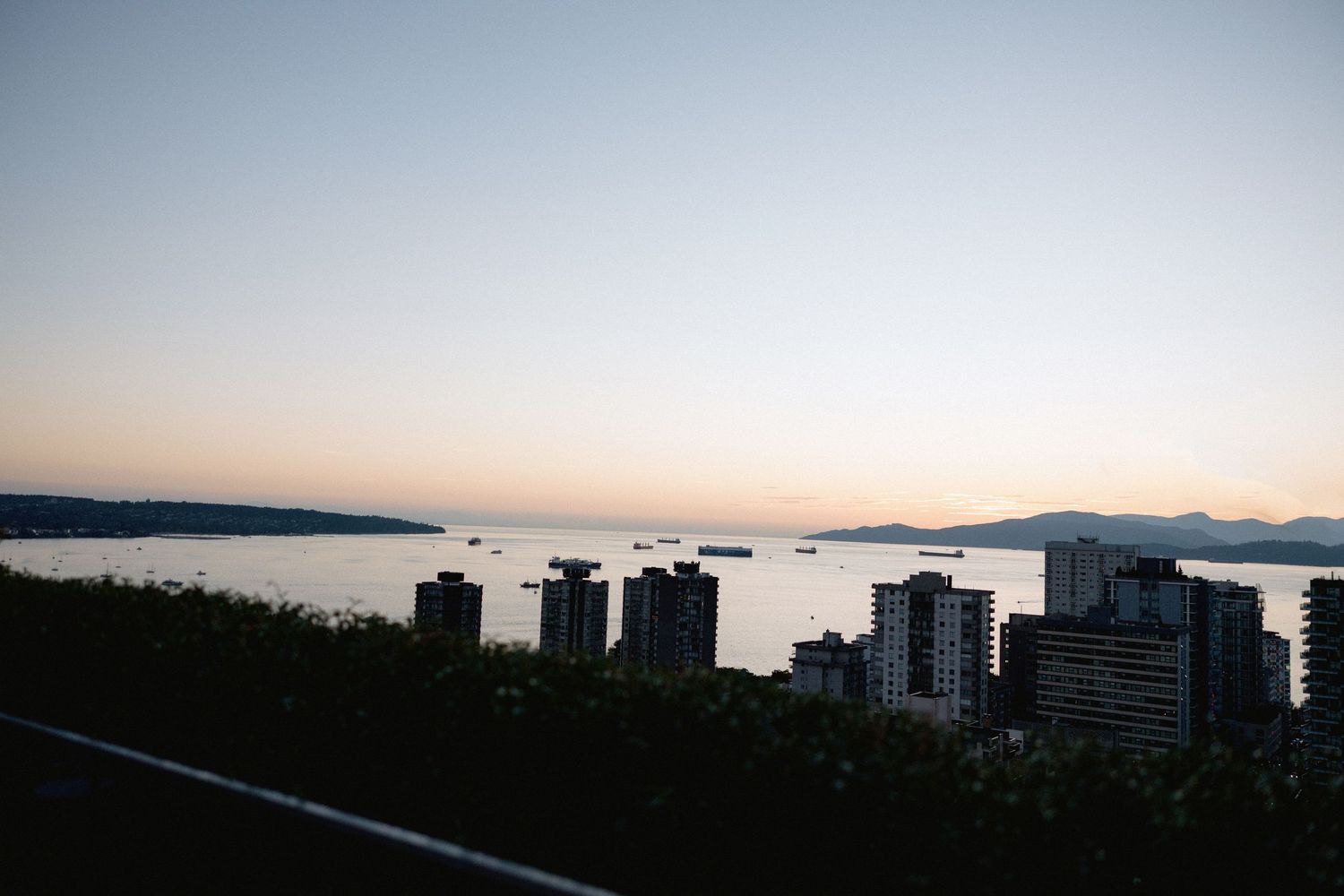 Panoramic sunset view of Vancouver's skyline with mountains and water in the distance.