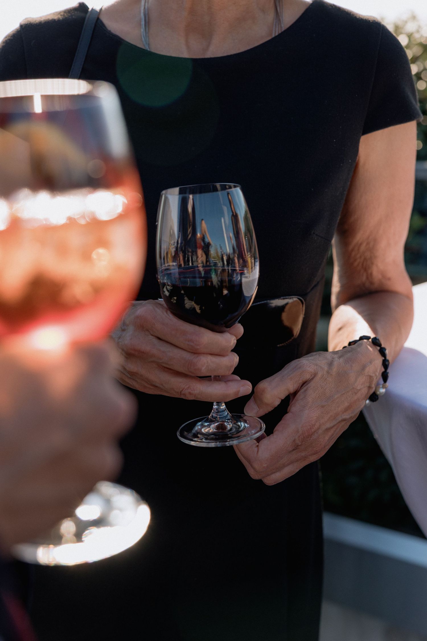 Person in black holding wine glasses during an evening event.