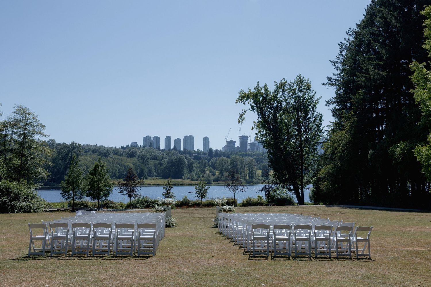 White chairs arranged in rows for an outdoor ceremony with city skyline views in the background at Hurt House in Burnaby
