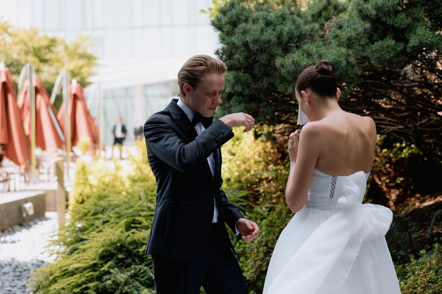 An emotional wedding first look moment captured in an urban garden setting with orange umbrellas.