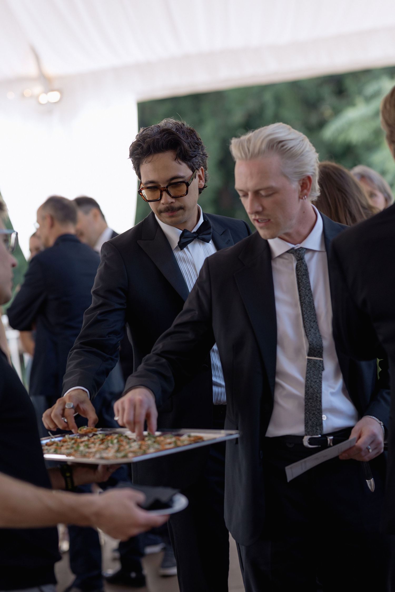 Wedding guests in formal attire gather around appetizer trays during the reception.