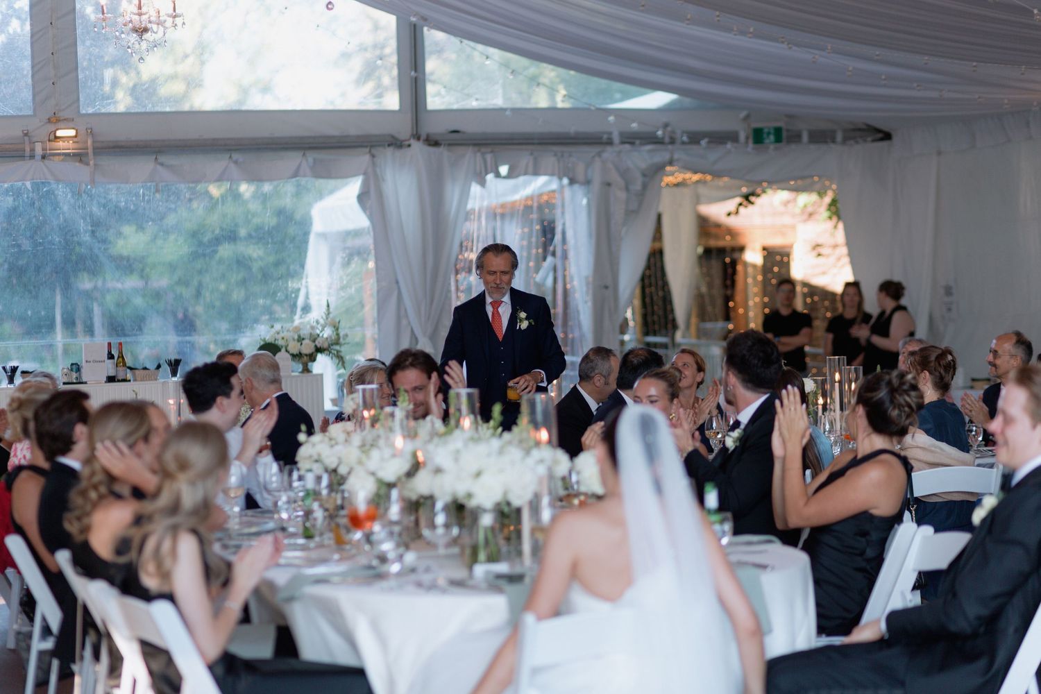 Large wedding tent decorated with string lights and white linens for an elegant reception.