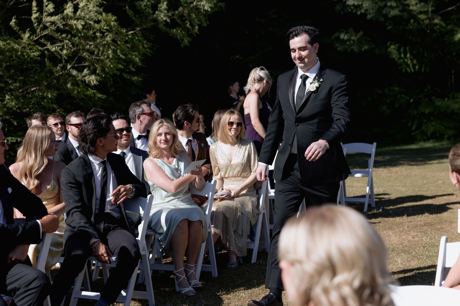 Guests arriving at an outdoor wedding ceremony with white chairs and natural backdrop.