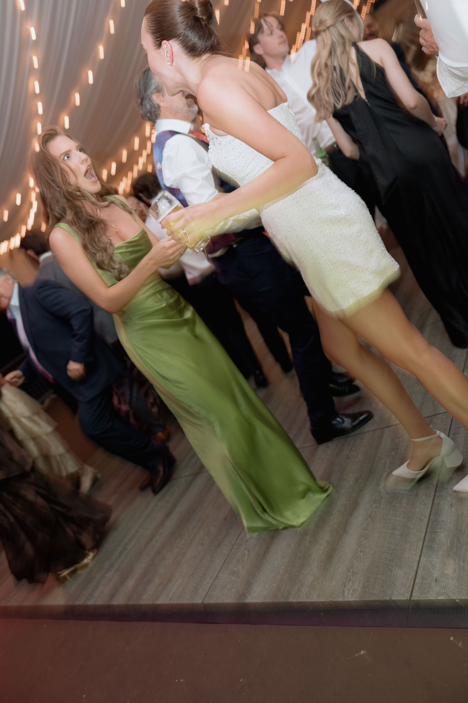Guests dancing in formal attire under twinkling lights at an indoor wedding reception.