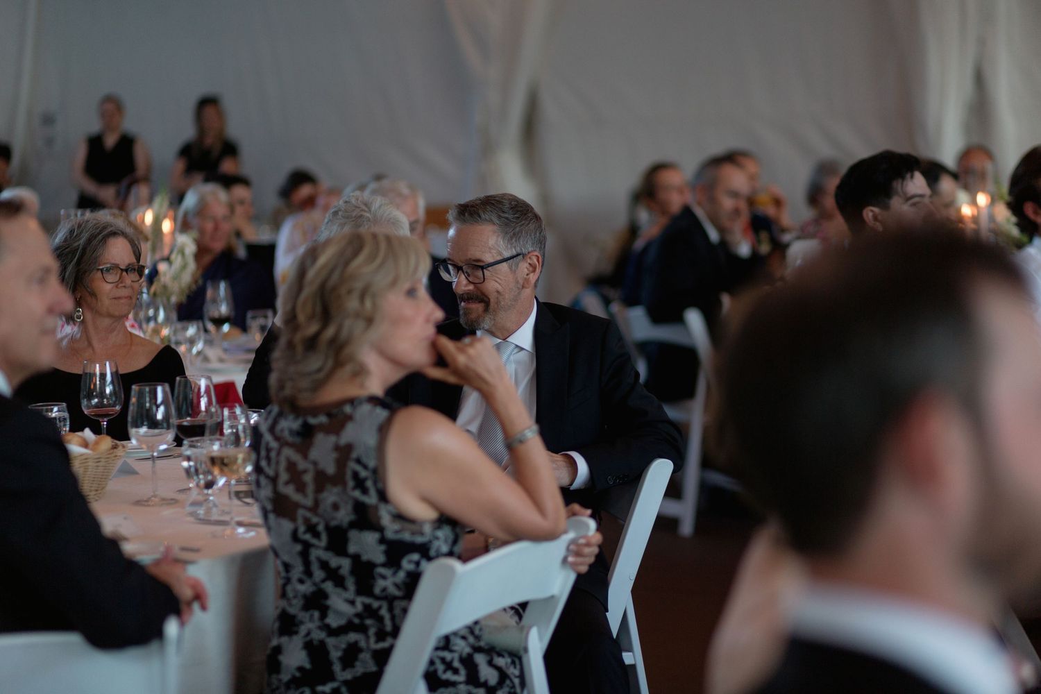 Formal reception guests enjoying dinner and speeches in an elegant tent setting.
