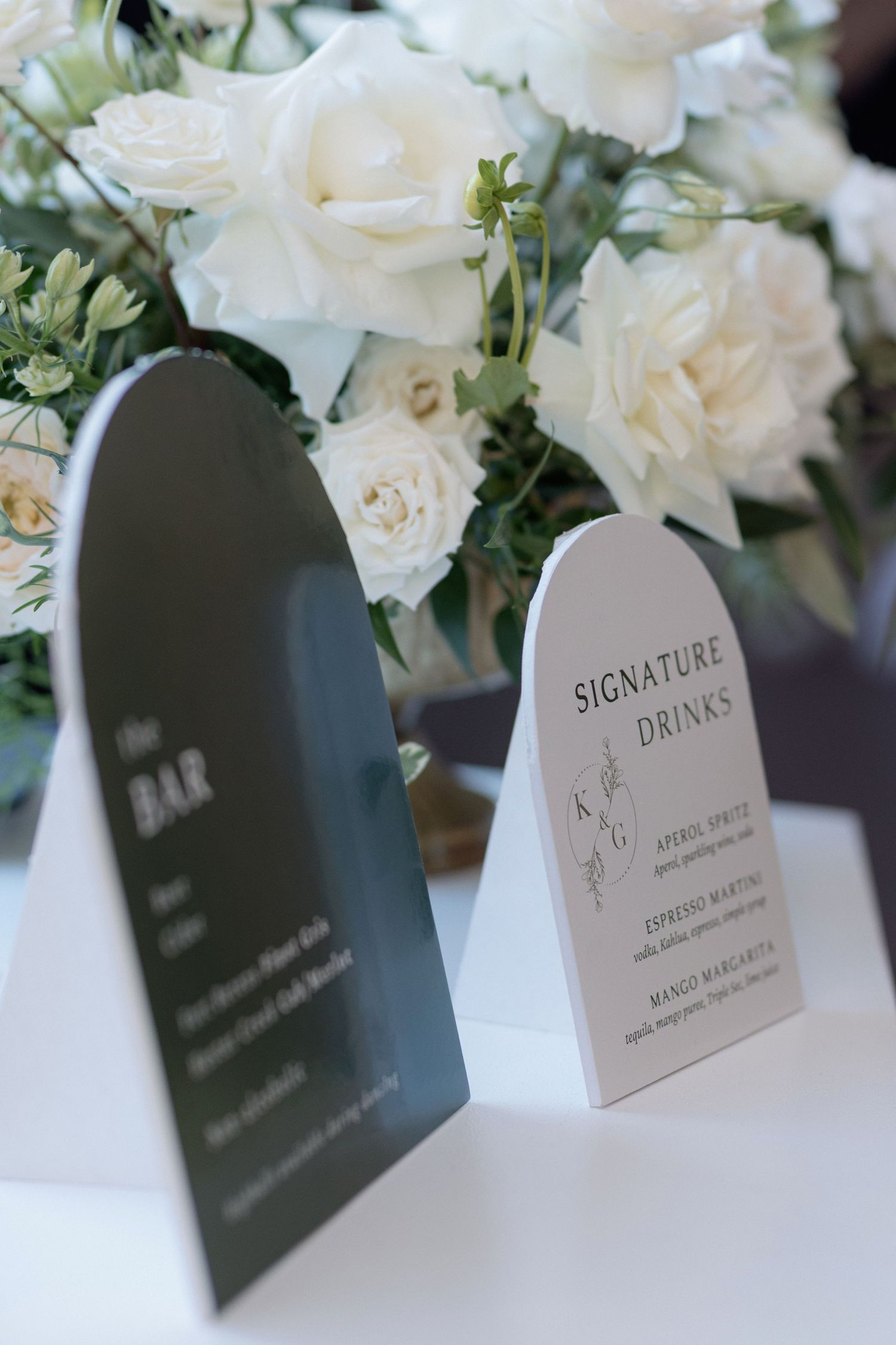 White signature drinks menu cards displayed with elegant white roses and greenery.