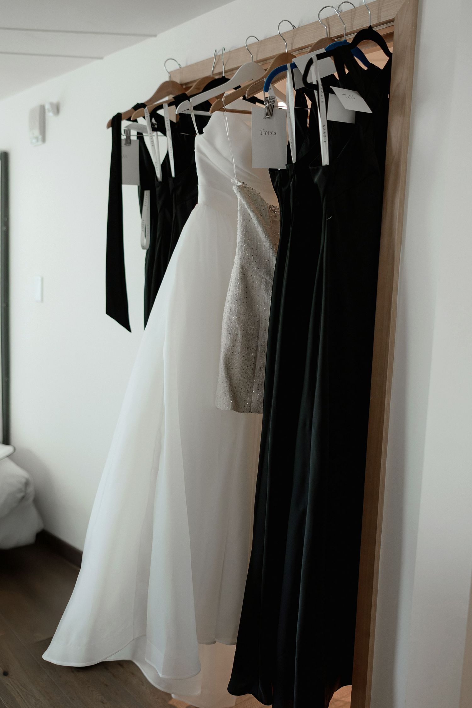 Wedding dresses and formal attire hanging on wooden hangers against a white wall.