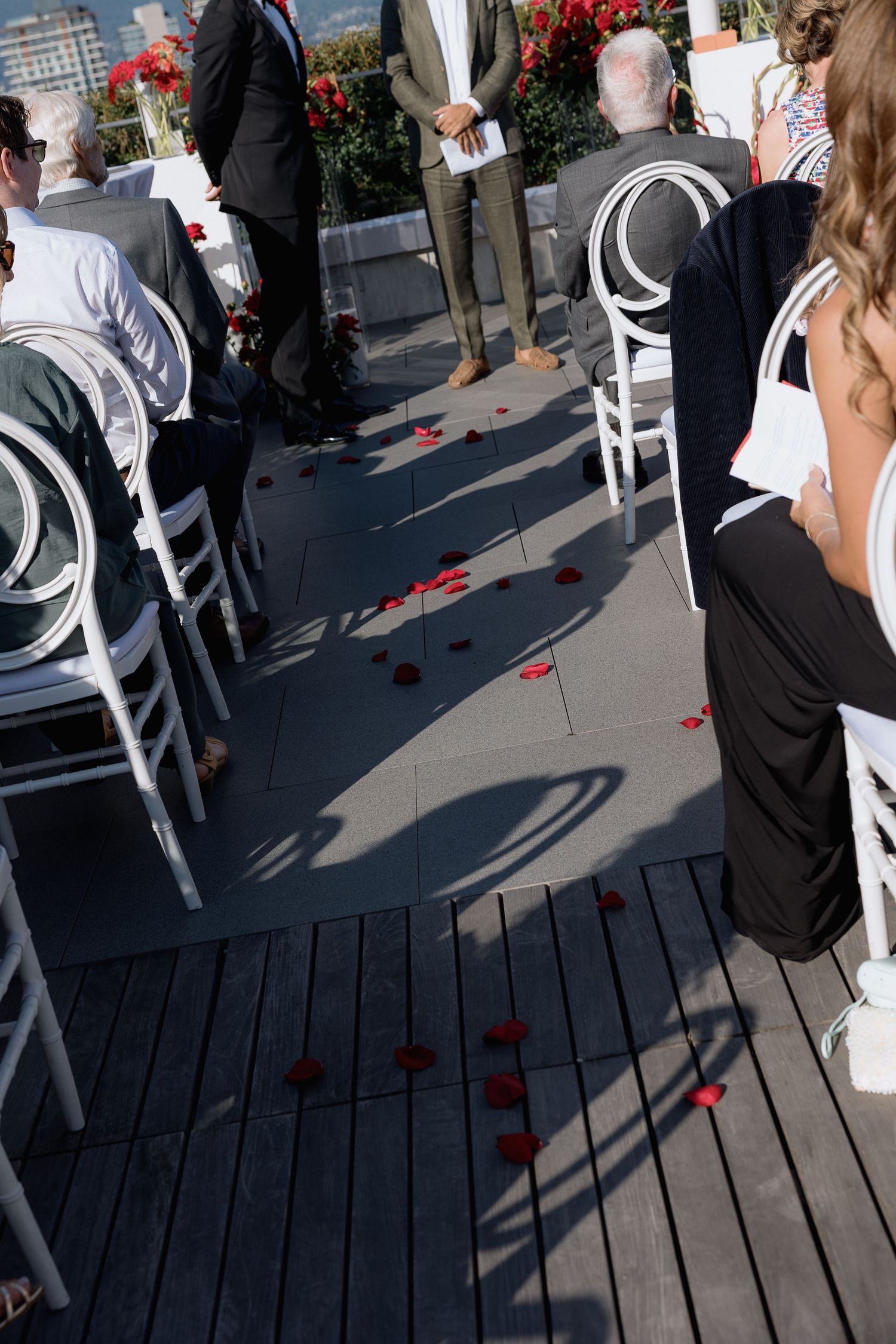 White chairs arranged on a wooden deck with scattered red rose petals creating a romantic atmosphere.