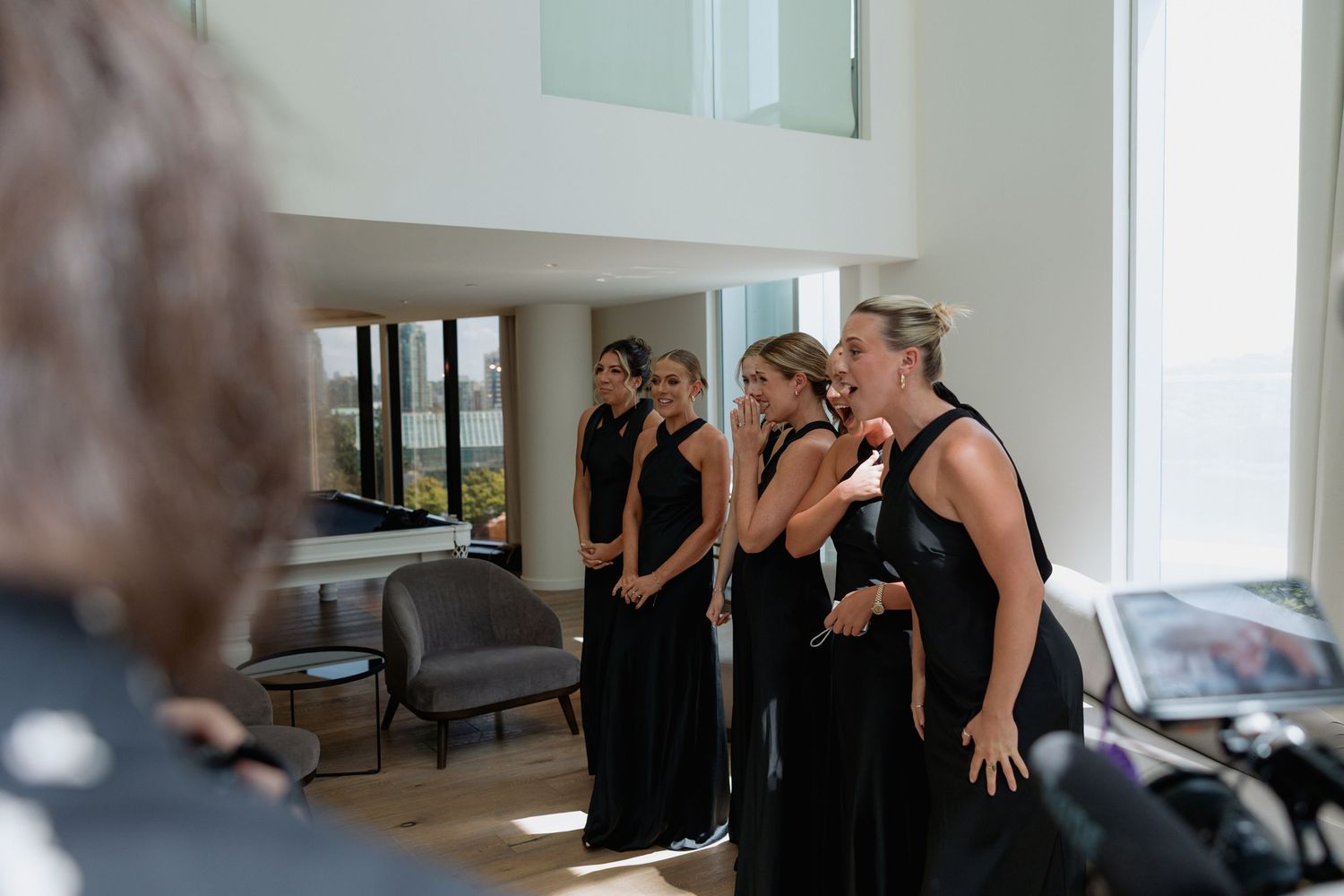 A group poses together in black dresses in a modern room with large windows.