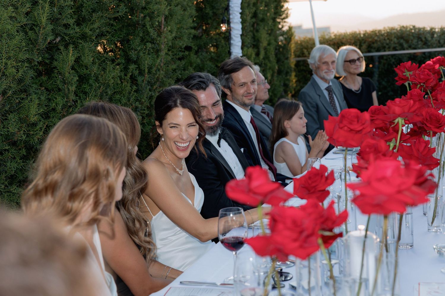 Wedding reception guests seated at tables decorated with bright red floral centerpieces.