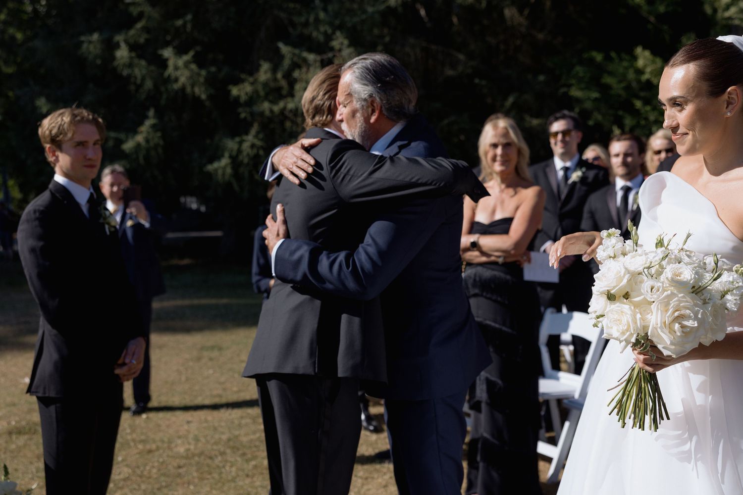 Wedding guests gather outdoors for a ceremony on a sunny day.