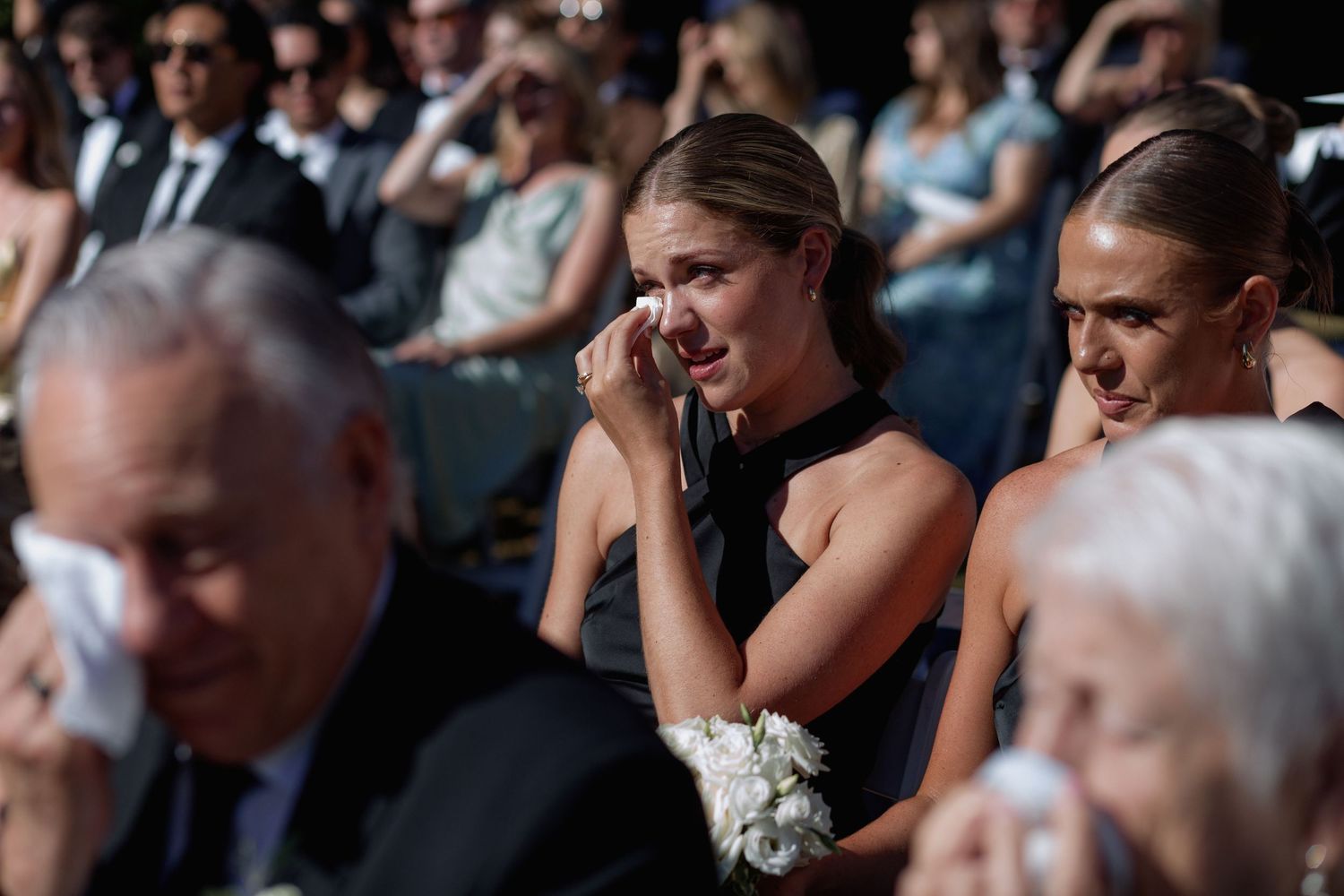 Wedding attendees in formal wear show emotional reactions during a touching moment at the ceremony.