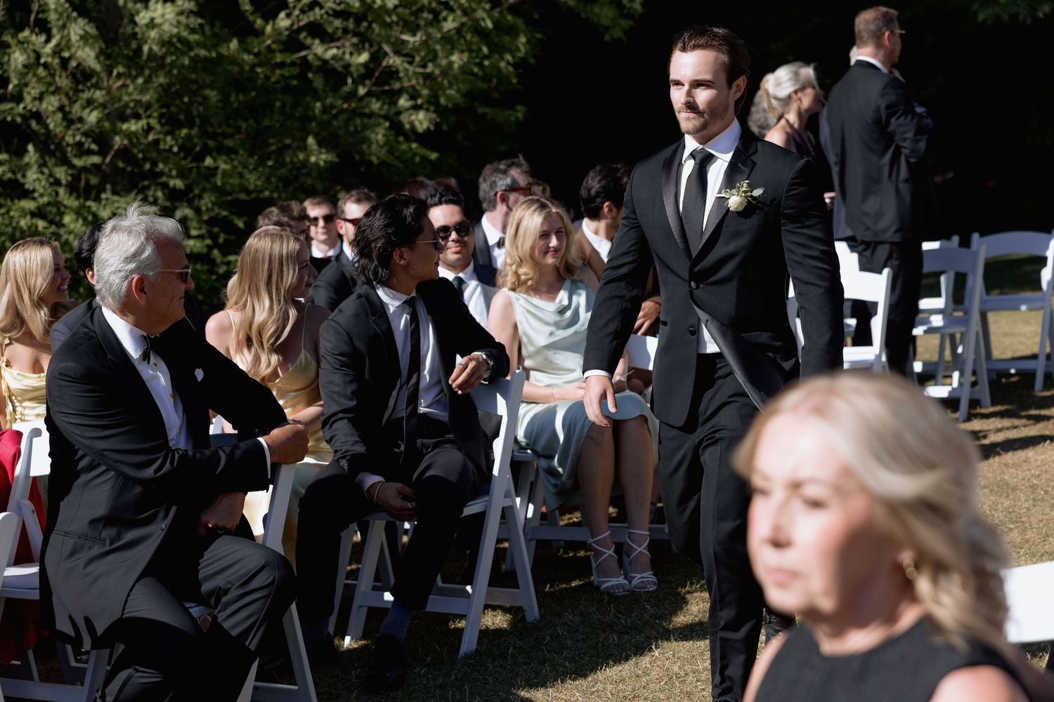 Wedding guests mingle before ceremony in an outdoor setting with white chairs.