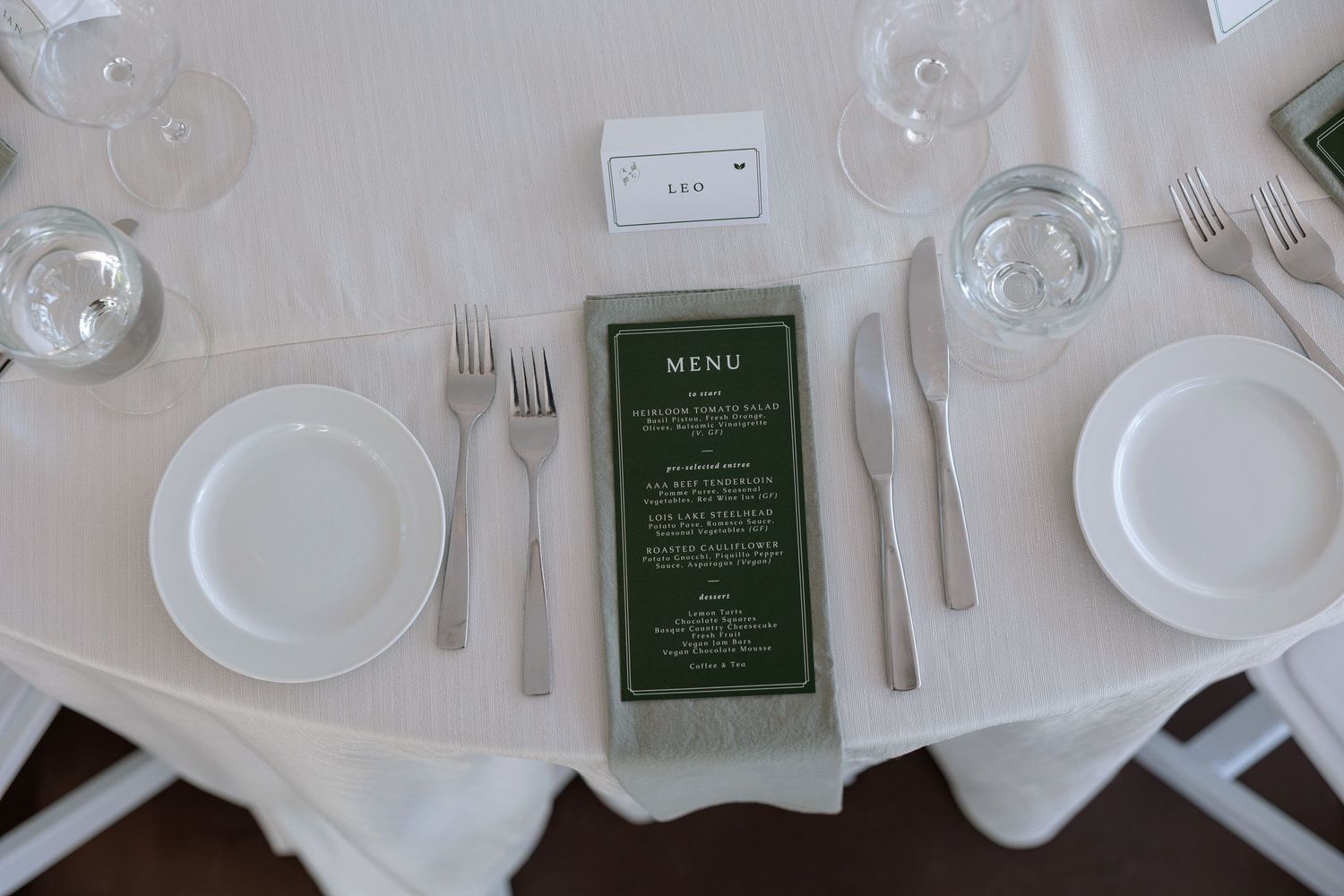 Overhead view of pristine white table settings with green menu cards and polished silverware.